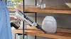A person is holding a cordless vacuum cleaner, demonstrating its use by pointing it towards a shelf. Anteprima dell’immagine prodotto