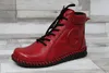 A red leather boot with black laces and sole, placed on a light gray and white wood-like background. Produktbild-Vorschau