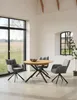 A dining set with a round wooden table and four chairs in a bright, modern room with large windows. Produktbild-Vorschau