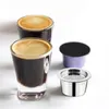 Two shot glasses filled with espresso are placed in front of a reusable coffee capsule and a metal coffee capsule holder. Produktbild-Vorschau