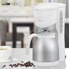 A coffee maker with a thermos carafe is shown on a table, with a cup of coffee and coffee beans nearby. The background is a blurred interior scene. Anteprima dell’immagine prodotto