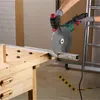 A person is using an angle grinder to cut a metal profile on a workbench. Produktbild-Vorschau