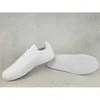 A pair of white Adidas sneakers are shown on a gray concrete background. One shoe is upright, and the other is lying on its side, showing the sole. Produktbild-Vorschau