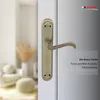 A close-up of a bronze door handle on a white door, with a blurred background of a room interior and marketing text on the right. Produktbild-Vorschau