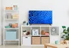 A living room setup with a TV on a shelf unit, next to a tall shelving unit filled with decorative items and storage boxes. Produktbild-Vorschau