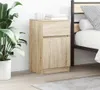 A wooden nightstand is placed next to a bed, with a plant in a pot on the left. Náhľad obrázku produktu