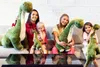 A group of people, including children, are sitting on a couch and holding large plush dinosaur toys. Náhled obrázku produktu