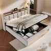 A bed with its storage compartment open, showing various items stored inside. The bed has a tufted headboard and a wooden shelf with a tablet and charging cables. Náhled obrázku produktu