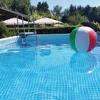 A beach ball floats in a swimming pool next to a ladder. Produktbild-Vorschau