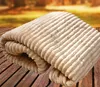 A folded blanket with a ribbed texture is placed on a wooden surface, with a blurred outdoor background suggesting autumn. Produktbild-Vorschau