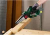 A hand wearing a glove is holding a cordless chainsaw and cutting a piece of wood. Produktbild-Vorschau