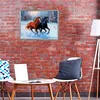 A painting of two horses running in the snow hangs on a brick wall above a small table with two chairs and pillows. Produktbild-Vorschau