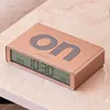A rose gold digital alarm clock with the word "on" embossed on its surface, placed on a marble-like surface. Anteprima dell’immagine prodotto