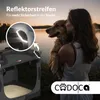 A woman holds a dog by a lake at sunset, with a dog transport box in the foreground. Produktbild-Vorschau