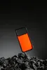 An orange and black phone case is shown floating above a pile of dark rocks against a dark background. Podgląd zdjęcia produktu