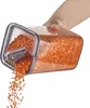 A hand is holding a clear plastic food storage container filled with red lentils, and the lentils are being poured out of the container. Produktbild-Vorschau