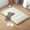 A cream-colored floor mattress is laid out on a wooden floor, with a black and white checkered blanket draped over it and an open book nearby. Náhľad obrázku produktu