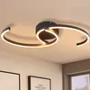 A modern ceiling light fixture with a swirling design, illuminating a room with framed artwork below. Náhled obrázku produktu
