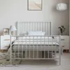 A white metal bed frame with a headboard and footboard, set up in a bedroom with nightstands and a rug. Náhled obrázku produktu