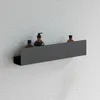 A black bathroom shelf mounted on a textured gray wall, holding two brown bottles. Produktbild-Vorschau