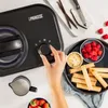 A hand is shown adjusting the dial on a black ice cream maker, surrounded by ingredients like raspberries, strawberries, vanilla beans, and wafer rolls. Produktbild-Vorschau