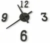 A close-up view of a black wall clock with large, three-dimensional numbers and black hands against a white background. Náhled obrázku produktu