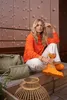A woman sits on a wooden bench holding a drink, with luggage and a lantern nearby. Voir les images du produit