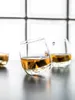 Three rocking whiskey glasses with whiskey and ice cubes on a dark surface, with a blurred background of white glass blocks. Podgląd zdjęcia produktu