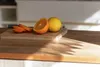 A cutting board with sliced oranges and a lemon on a wooden countertop, with sunlight casting shadows. Anteprima dell’immagine prodotto