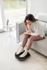 A woman is sitting on a couch with her feet on a massage device. Produktbild-Vorschau
