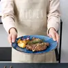 A person wearing an apron is holding a blue plate with a meal on it. Náhled obrázku produktu