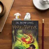 A Harry Potter book with two character-themed bookmarks on top, a cup of coffee and a pencil on the side, all on a wooden table. Produktbild-Vorschau