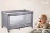 A baby is lying on a blanket next to a travel crib. Podgląd zdjęcia produktu