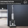 A white vacuum cleaner is shown in its charging dock against a dark blue wall and a kitchen background. Text overlays advertise it as a docking station for convenient storage and charging. Produktbild-Vorschau