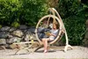 A woman reads a book while sitting in a hanging egg chair in a garden. Produktbild-Vorschau