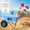 A blue children's wheelbarrow on a sandy beach with a person in the ocean in the background and sandcastles. Produktbild-Vorschau