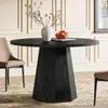 A round black dining table with a unique pedestal base, set in a dining room with a chair and decorative items on the table. Produktbild-Vorschau