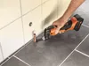 A person is using a power tool to cut a copper pipe near a tiled wall and floor. Produktbild-Vorschau