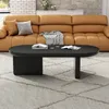A modern living room scene featuring a sleek black oval coffee table placed on a textured rug in front of a stylish caramel-colored sofa. Voir les images du produit
