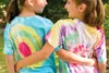 Two young girls are standing outside with their arms around each other, wearing tie-dye shirts. Produktbild-Vorschau