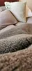 A close-up view of a textured blanket with pillows in the background. Produktbild-Vorschau