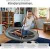 A young boy is sitting on a round swing in a child's room, with shelves of toys and a desk in the background. Anteprima dell’immagine prodotto