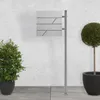A modern mailbox with a newspaper compartment mounted on a silver stand, placed outdoors next to a potted plant and a topiary. Náhled obrázku produktu