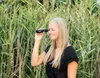 A woman is looking through binoculars in a field of tall grass. Produktbild-Vorschau