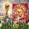 A collection of football-themed figurines and a large trophy are displayed on a green field, with a stadium in the background and a promotional calendar box. Produktbild-Vorschau