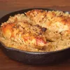 A close-up shot of a cast iron skillet filled with cooked rice and topped with seasoned chicken breasts. Anteprima dell’immagine prodotto