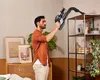 A man is using a cordless vacuum cleaner to clean a shelf in a room. Produktbild-Vorschau