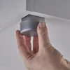 A hand is shown attaching a gray furniture foot to the underside of a white surface. Produktbild-Vorschau