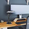 A black desk lamp with a fan and phone holder is on a wooden desk next to a computer monitor. Náhľad obrázku produktu