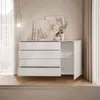 A modern white dresser with four drawers and a cabinet with an open door, displayed in a well-lit room with artwork on the wall and curtains in the background. Produktbild-Vorschau